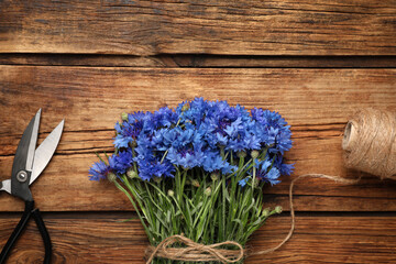 Bouquet of beautiful cornflowers with scissors and twine on wooden table, flat lay