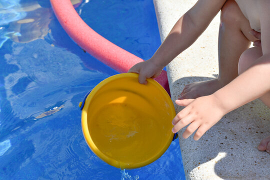 Manos de ni&ntilde;o jugando con cubo amarillo de agua en la piscina