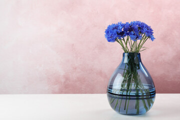 Bouquet of beautiful cornflowers in glass vase on light table. Space for text