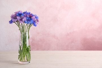 Bouquet of beautiful cornflowers in glass vase on white wooden table. Space for text