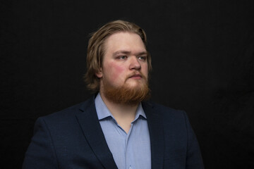 Portrait of a serious man 25-30 years old with a red beard on a dark background, looking away, overweight.