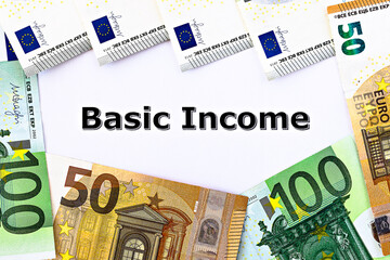 Topview photo on Universal Basic Income theme. The words Basic Income on paper, surrounded by euro banknotes