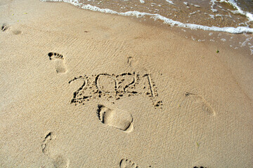 End of year 2021, lettering on the beach with sea wave. Numbers 2021disappear on the sea shore, message handwritten in the sand