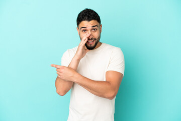 Young arab man isolated on blue background pointing to the side to present a product and whispering something