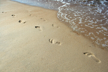 Footprints in the sand with sea wave. Summer travel concept, copy space