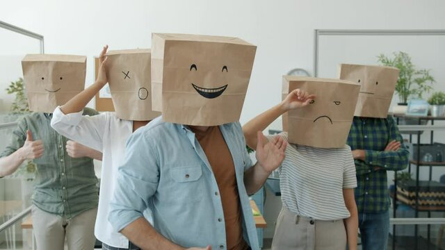 Slow motion portrait of funny office workers wearing paper bags with emoji pictures expressing emotions standing in workplace together. Job and people concept.