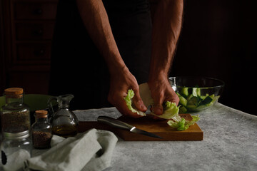 a man tears cabbage with his hands. Cooking a green vegetable salad on a dark background. Dark photo. Low Key