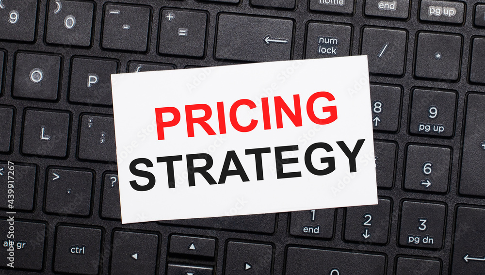 Poster on a black computer keyboard there is a white card with the text pricing strategy. view from above