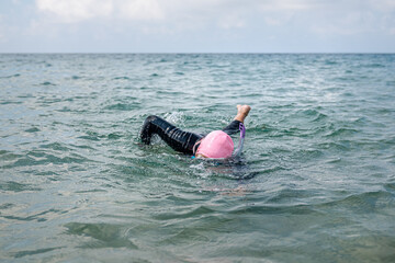 Woman in wetsuit with snorkeling goggles and pink swim cap swimming in the sea.