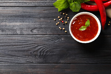 Spicy chili sauce and ingredients on dark wooden table, flat lay. Space for text