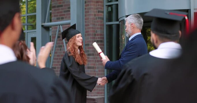 Great moment. Full length view of the teacher giving diploma to the student girl wearing graduation gown and hat. Girl and her group mates rejoicing and celebrating