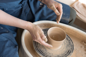 hands of a potter making ceramic mug from clay on pottery wheel