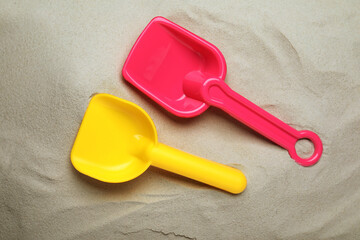 Bright plastic toy shovels on sand, flat lay