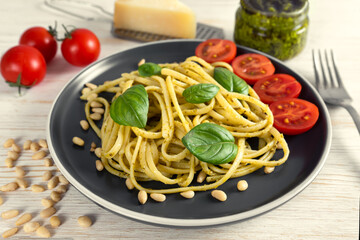 Pasta pesto with fork on white wooden background. Traditional italian spaghetti with food ingredients pesto sauce, tomato, parmesan cheese, pine nuts, fresh basil leaves