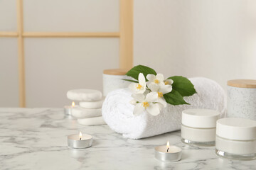 Composition with beautiful jasmine flowers and skin care products on white marble table indoors, space for text