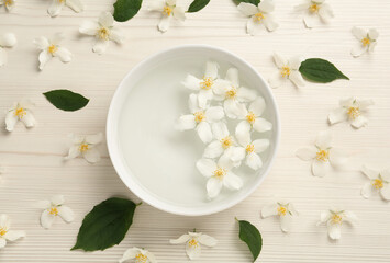 Fototapeta na wymiar Bowl with water and beautiful jasmine flowers on white wooden table, flat lay