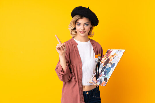 Young Artist Girl Holding A Palette Isolated On Yellow Background Touching On Transparent Screen