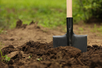 Shovel in soil outdoors, space for text. Gardening tool