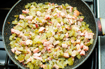 Frying ingredients for making a hodgepodge. Various types of sausages and meats and pickles are fried in a pan.