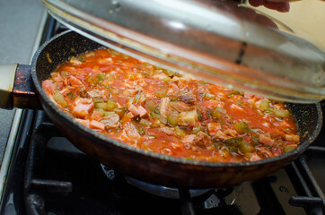 Various types of sausages and meats and pickles are fried in a pan.