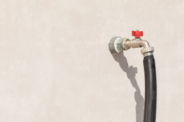 Water tap with red valve and hose, from outer, street wall of building, house. Equipment for watering lawns and flower beds, plant care.