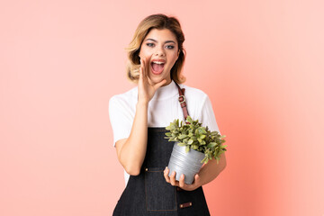 Russian gardener girl holding a plant isolated on pink background shouting with mouth wide open