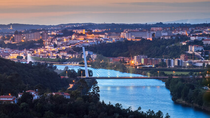 Fototapeta premium Panoramic view of Coimbra at dusk, in Portugal, with the Mondego river and the Rainha Santa Isabel bridge in the foreground and the university with its tower in the background.