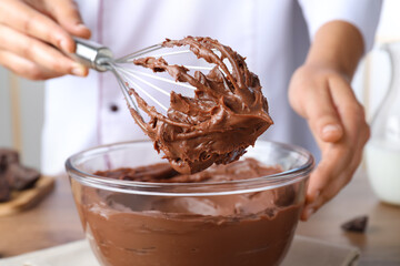 Professional confectioner whipping chocolate cream with balloon whisk at table, closeup