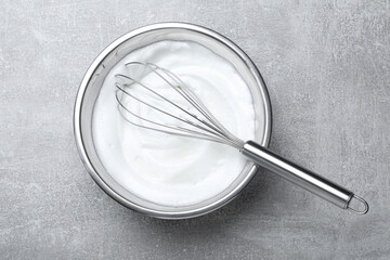 Whipped egg whites with balloon whisk on grey table, top view