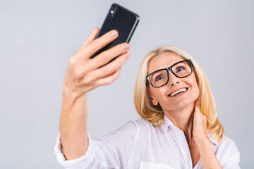 Fototapeta premium Happy mature senior woman holding smartphone using mobile online apps, smiling old middle aged lady texting sms message chatting on phone looking at cellphone isolated on white grey background