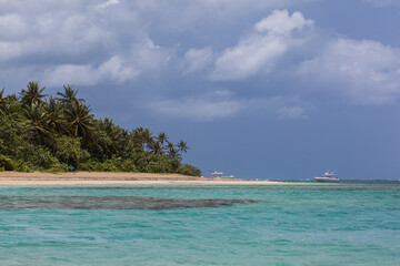 Dramatic image of the Caribbean coast with turquoise blue water in foreground and palms on the coast with fishing boats in the background.