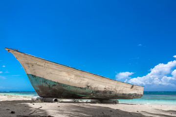 Fototapeta na wymiar Dramatic image of a old wooden weathered fishing boat on the Caribbean coast with turquoise blue water in the background and white sandy beach.