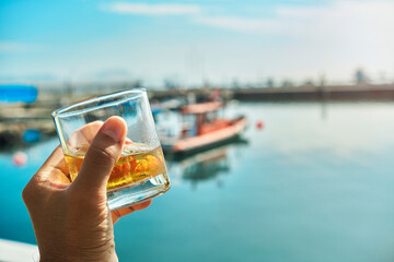 Male hand holding glass whiskey the beginning of summer at marina, summer concept