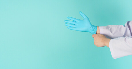 Doctor hands is pulling blue latex glove on green mint OR tiffany blue background.He wear long...