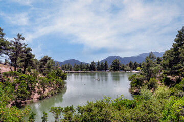 Panoramic view to Beletsi Lake and the beautiful nature that surrounds the lake. It is located at an altitude of 600 meters on Parnes mountain in Athens, Greece. Sunny day, cloudy blue sky