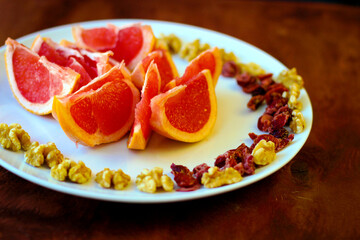 Naklejka na ściany i meble Wonderful vegan food: grapefruit sliced with slices, walnut kernels, dried cranberries stand on a white plate