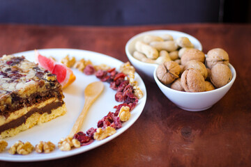 Piece of tasty chocolate-nut cake on a white plate. Walnuts and wooden spoon stand nearby