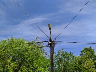 electric pole with wires against the blue sky and green trees