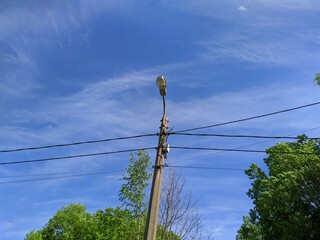 electric pole with wires against the blue sky and green trees