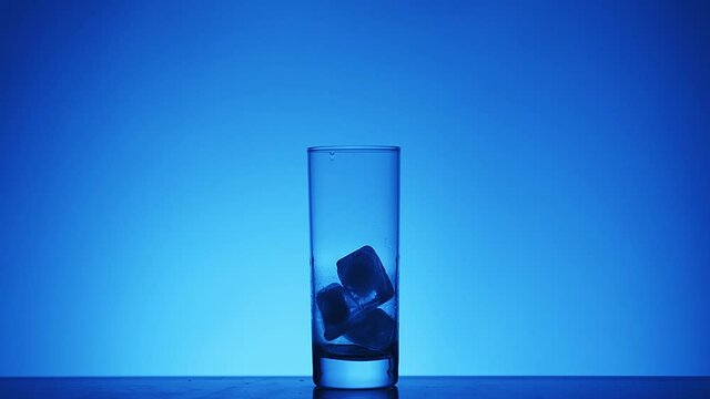 Ice Cubes Falls Into A Collins Glass On The Blue Background. Silhouette.