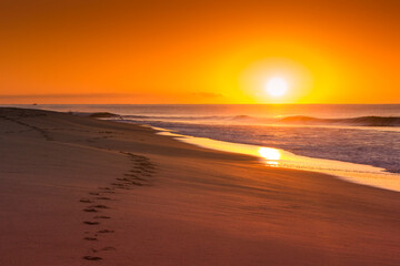 Fototapeta na wymiar amanecer en la playa con huellas en la arena