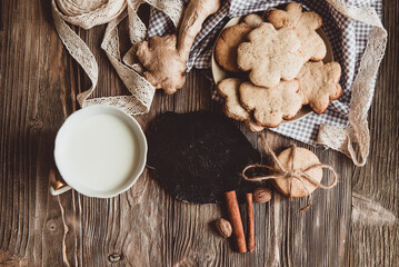 Close up of homemade ginger cookies, cinnamon, ginger with cup of milk on a towel wooden table. Copy space. Retro toned image, flat lay
