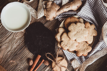 Close up of homemade ginger cookies, cinnamon, ginger with cup of milk on a towel wooden table. Copy space. Retro toned image, flat lay