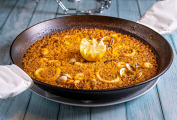 Food photography of seafood paella with rice, squid, prawns, mussels, and shells on a restaurant. Typical spanish meal on a wooden table.