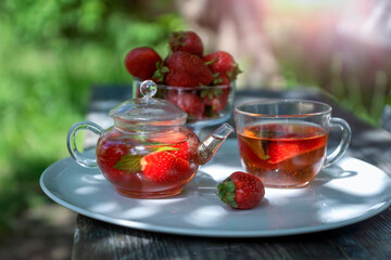 Fruit red tea with strawberries and mint leaves in the summer garden.