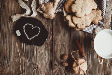 Close up of homemade ginger cookies, cinnamon, ginger with cup of milk on a towel wooden table. Copy space. Retro toned image, flat lay