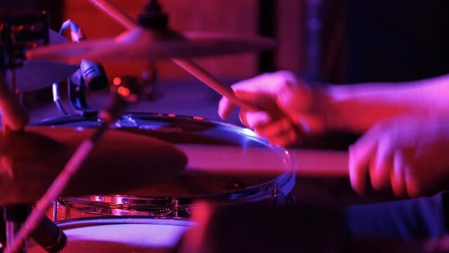 Man drummer playing on a drums on a rock concert in a club. Red lighting, closeup.