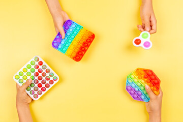 Many hands holding colorful pop it fidget toys on yellow background. Push pop-it fidgeting game helps relieve stress, anxiety, autism, provide sensory and tactile experience for children