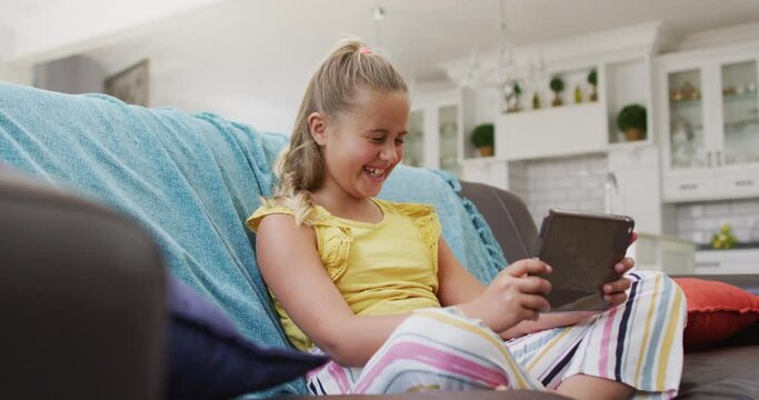 Happy caucasian girl at home, sitting on couch using tablet and smiling