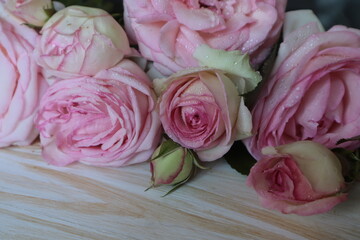 A beautiful bouquet of pink roses lies on a light wooden surface.	